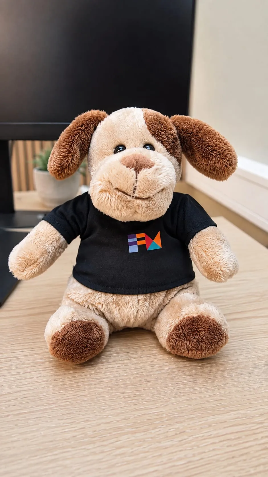 A plush dog wearing a t-shirt with the FM CyberSecurity logo, on a desk in the office